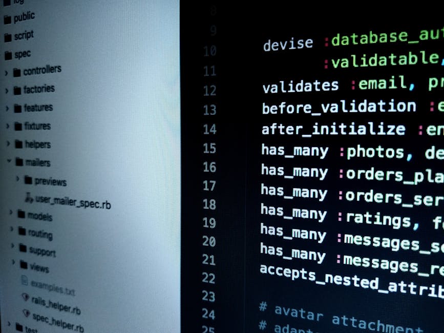 A person working on a laptop with a dark screen displaying lines of code in green, blue, and white text. The laptop has a silver body and a black keyboard, positioned on a dark surface. The individual